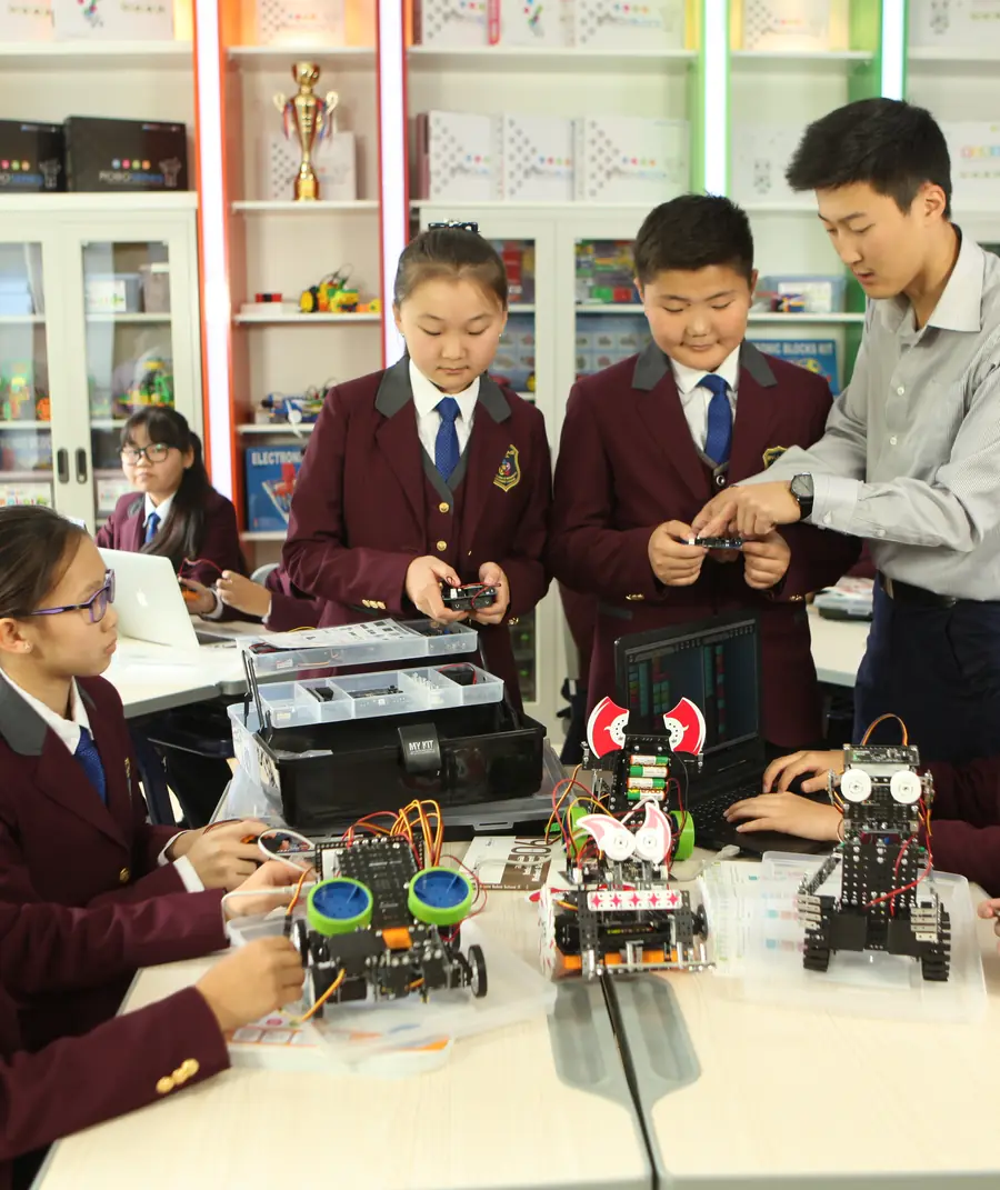 Students in maroon Oyunlag blazers build and program robots with their teacher